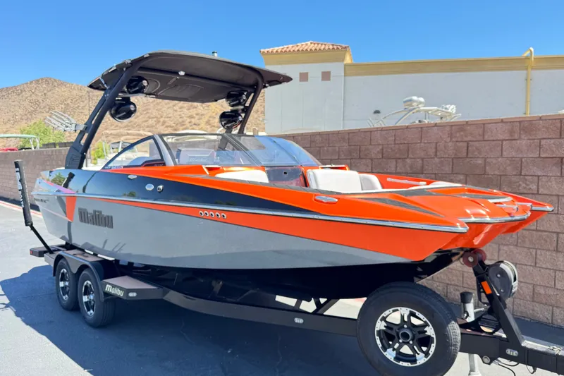 Slide: The Image of 2018 Malibu Wakesetter 22 MXZ boat with vibrant orange and gray design on a trailer. - 1