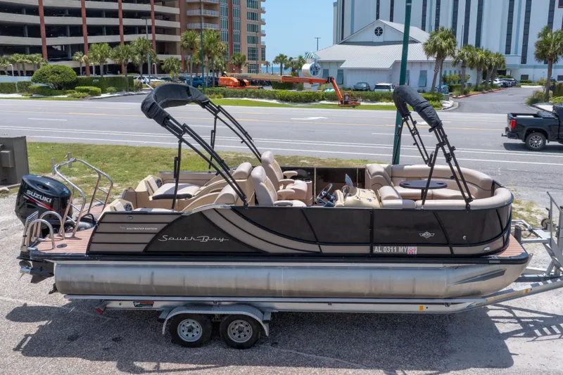 Slide: The Image of 2017 South Bay 523SL pontoon boat on trailer, parked near road with buildings in background. - 3
