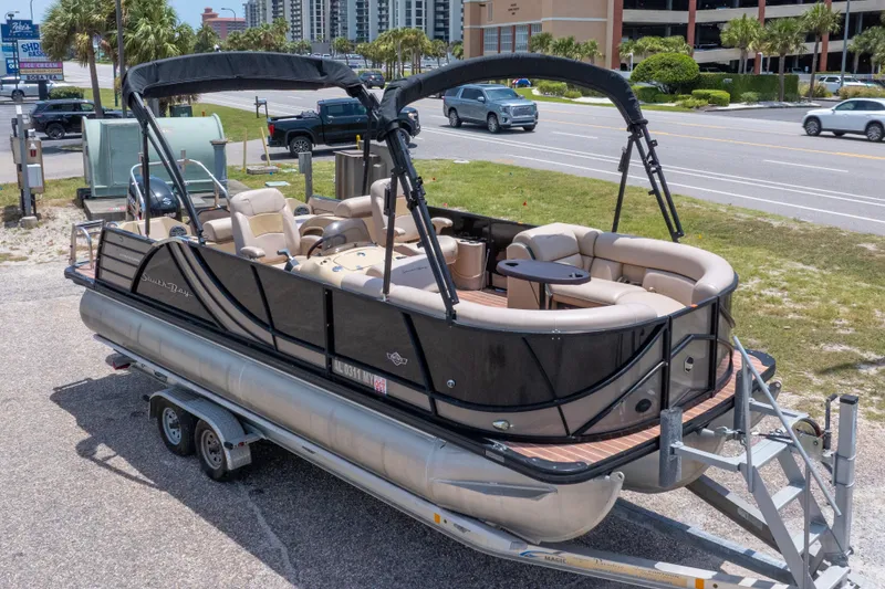 Slide: The Image of 2017 South Bay 523SL pontoon boat on trailer, parked near a road with palm trees. - 2