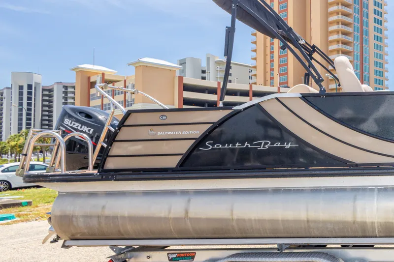Slide: The Image of 2017 South Bay 523SL pontoon boat with Suzuki engine, parked near modern buildings. - 40