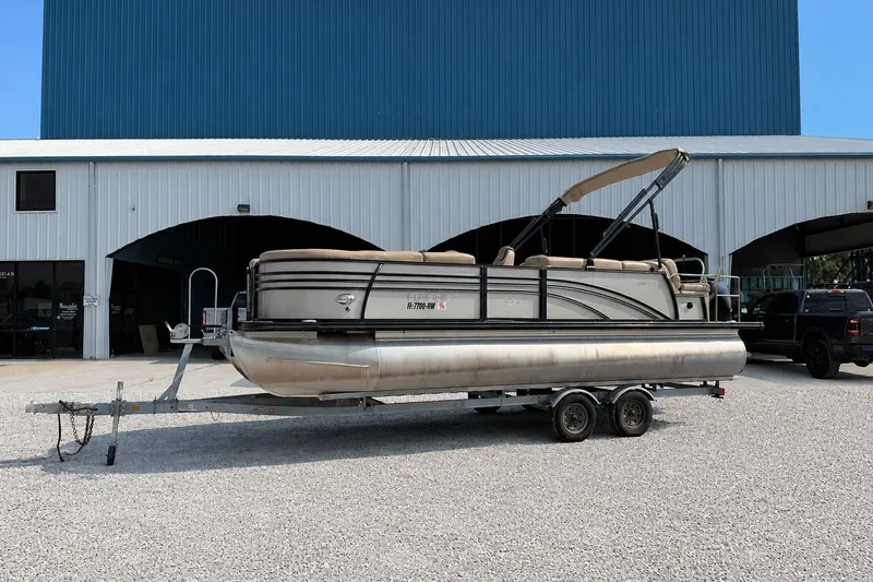 The Image of 2019 Harris Sunliner 230 pontoon boat on trailer, parked outside a large blue building. - 0