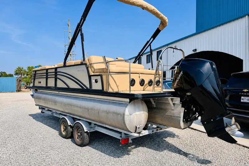 Slide: The Image of 2019 Harris Sunliner 230 pontoon boat on trailer, parked outside a blue building. - 7