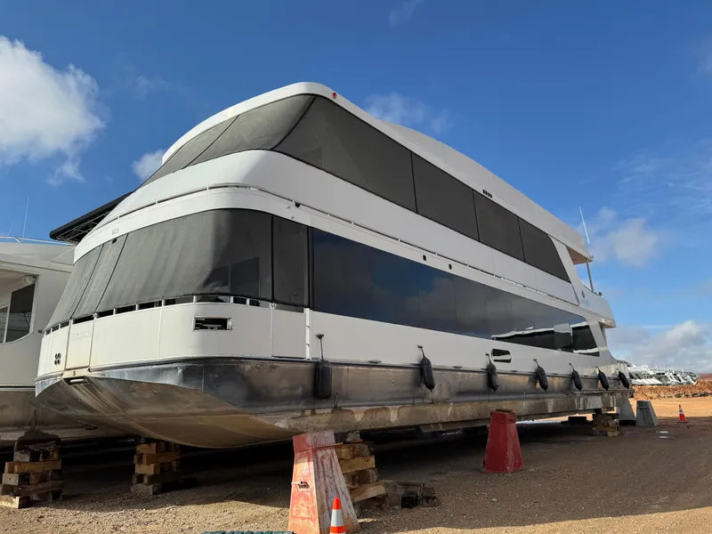 Slide: The Image of Houseboat Adonia Solace Trip #16, 2021 model, elevated on blocks under a clear blue sky. - 1
