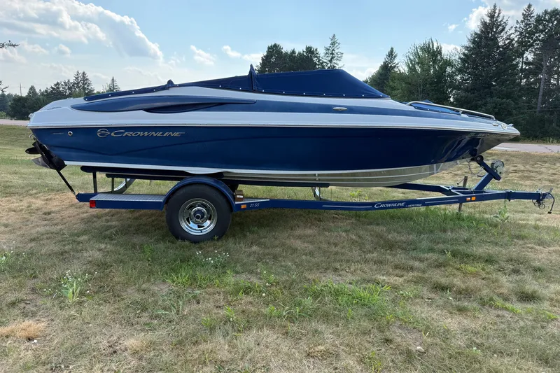 Slide: The Image of 2013 Crownline 21 SS boat on trailer, parked on grassy field with trees in background. - 6