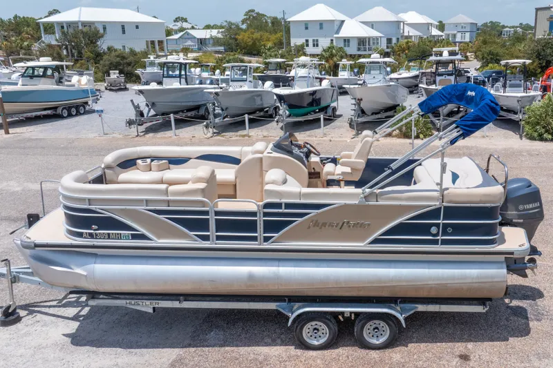 Slide: The Image of 2014 Aqua Patio 22 SLC pontoon boat on trailer, parked near other boats. - 3