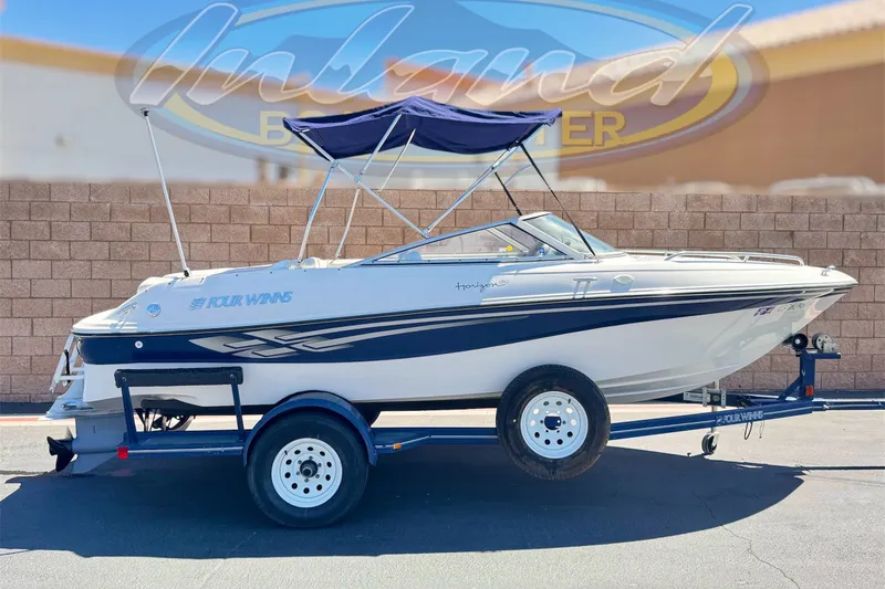 The Image of 2001 Four Winns 180 Horizon boat on trailer with blue canopy, parked outdoors. - 0