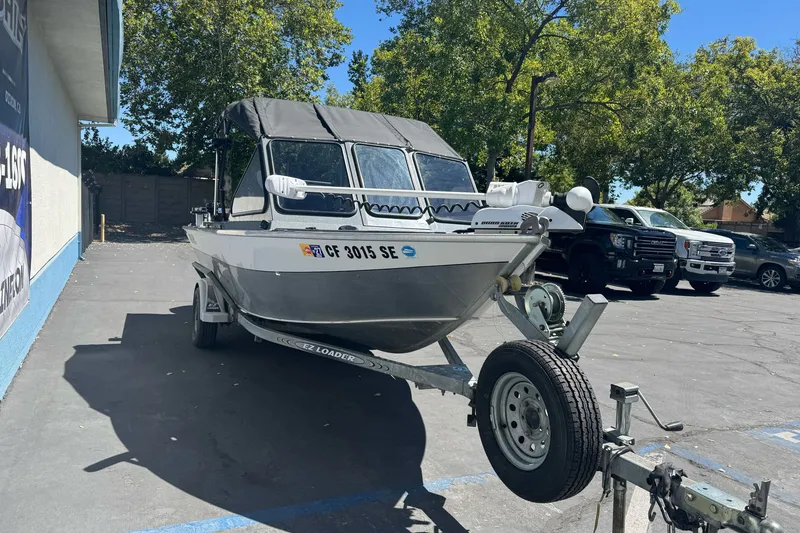 Slide: The Image of 2000 North River 18 Mariner boat on trailer in parking lot, surrounded by trees and vehicles. - 3