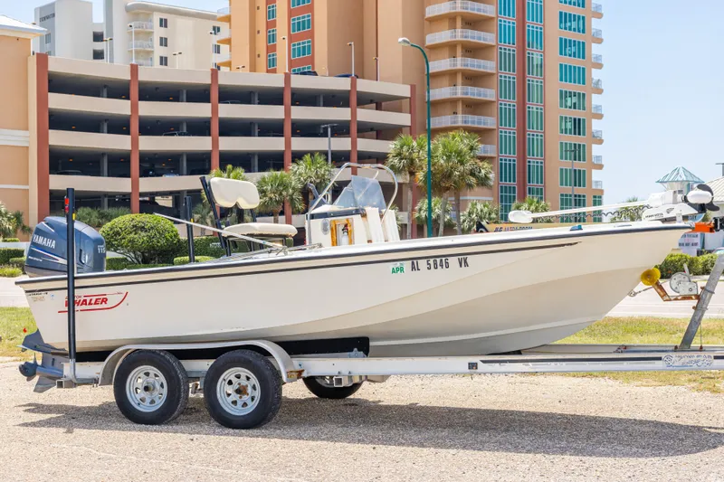 The Image of 1986 Boston Whaler 18 Outrage boat on trailer, parked near modern buildings. - 0
