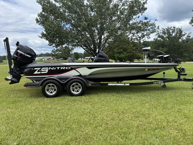 Slide: The Image of A 2011 Nitro Z9 CDC boat on a trailer, parked on a grassy field, with trees in the background. - 2