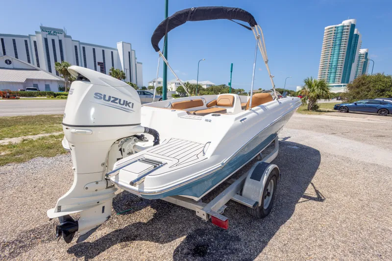 Slide: The Image of 2021 Stingray 182 SC boat with Suzuki outboard motor on trailer, parked near modern buildings. - 14