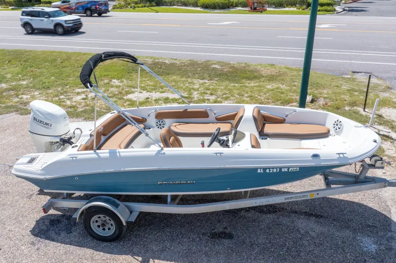 Slide: The Image of 2021 Stingray 182 SC boat on trailer with Suzuki outboard motor, parked near road. - 2