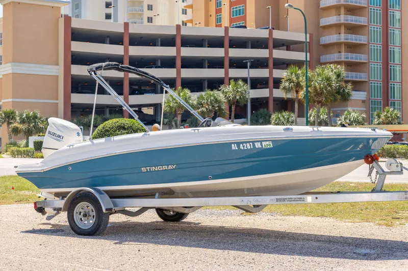The Image of 2021 Stingray 182 SC boat on trailer, parked near modern buildings and palm trees. - 0