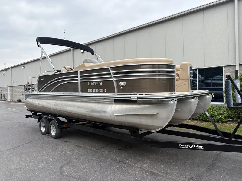 Slide: The Image of A 2019 Harris Sunliner 230 pontoon boat on a trailer in front of a building. - 2