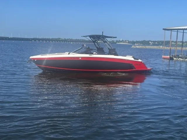 The Image of A 2022 Cobalt R8 Surf boat on calm water, featuring a red and black hull. - 1