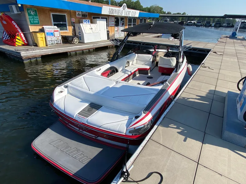 Slide: The Image of A 2012 Malibu 247 LSV boat docked. It features a white and red design with a black canopy. - 4