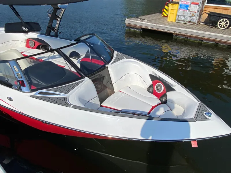 Slide: The Image of A 2012 Malibu 247 LSV boat with white and red interior, docked by the water. - 3