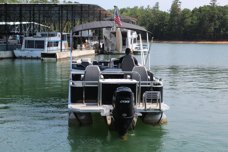 Slide: The Image of A 2024 Avalon LSZ RF 2585 pontoon boat on a calm lake with a covered dock in the background. - 5