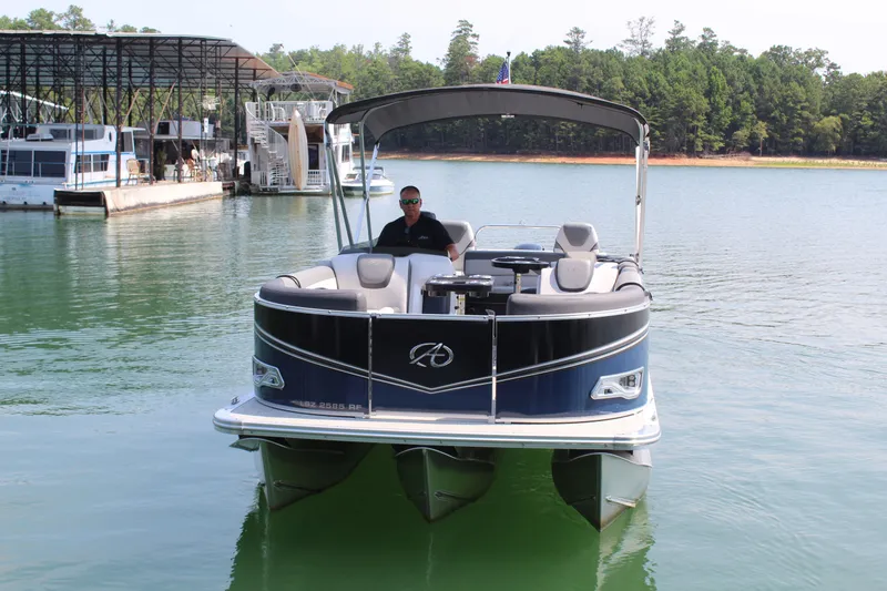 Slide: The Image of A 2024 Avalon LSZ RF 2585 pontoon boat on a calm lake, with a driver on board. - 4
