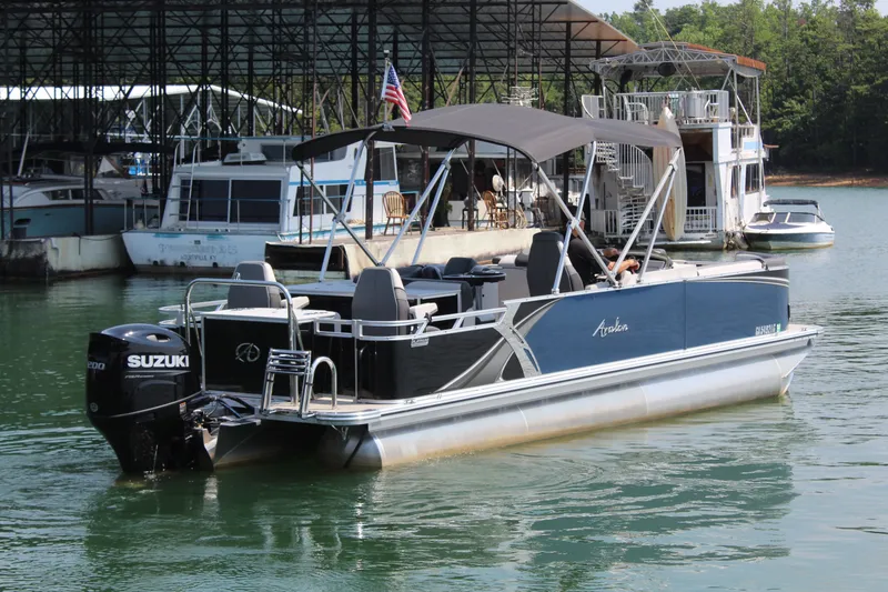 Slide: The Image of A 2024 Avalon LSZ RF 2585 pontoon boat with a black canopy and Suzuki outboard motor on a lake. - 7