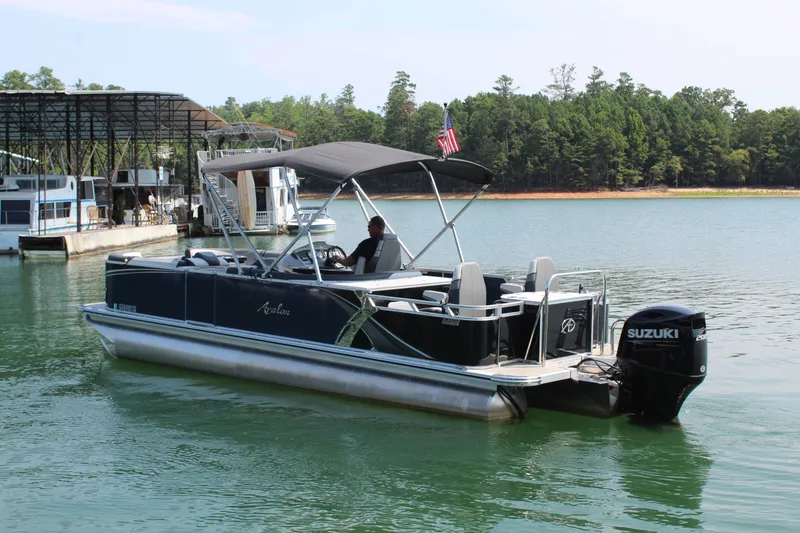 Slide: The Image of A 2024 Avalon LSZ RF 2585 pontoon boat with a black canopy and Suzuki outboard motor on a lake. - 3