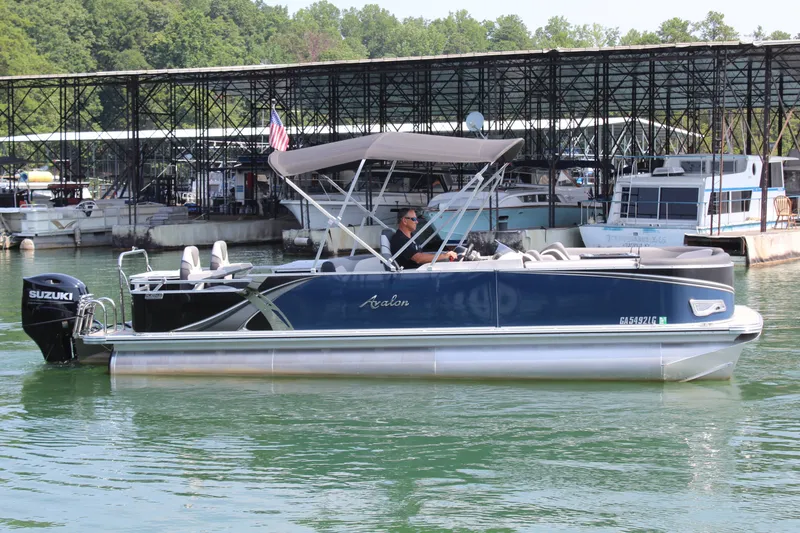 Slide: The Image of A 2024 Avalon LSZ RF 2585 pontoon boat on calm water, featuring a Suzuki outboard motor. - 6