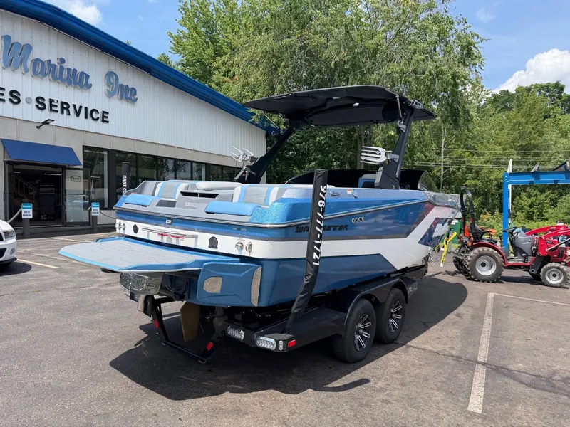Slide: The Image of A blue 2025 Malibu Wakesetter 22 MXZ on a trailer in front of a building. A tractor is visible in the background. - 8
