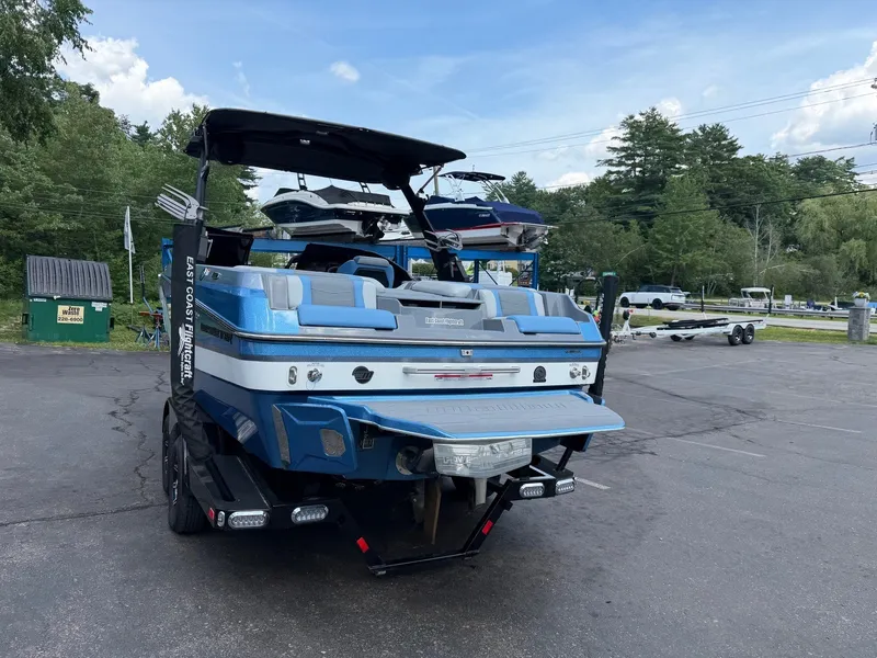 Slide: The Image of A blue 2025 Malibu Wakesetter 22 MXZ is parked on a lot. Trees and boats are visible in the background. - 12