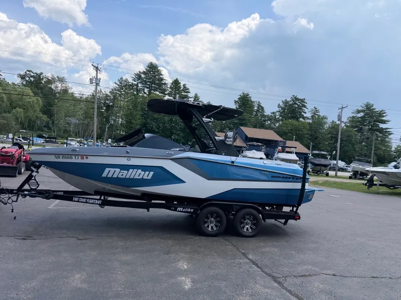 Slide: The Image of A blue and white 2025 Malibu Wakesetter 22 MXZ sits on a trailer in a parking lot. - 14