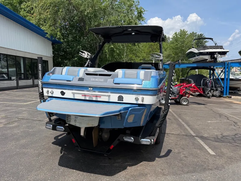 Slide: The Image of A blue 2025 Malibu Wakesetter 22 MXZ is parked in a lot. Trees and another boat are visible in the background. - 10