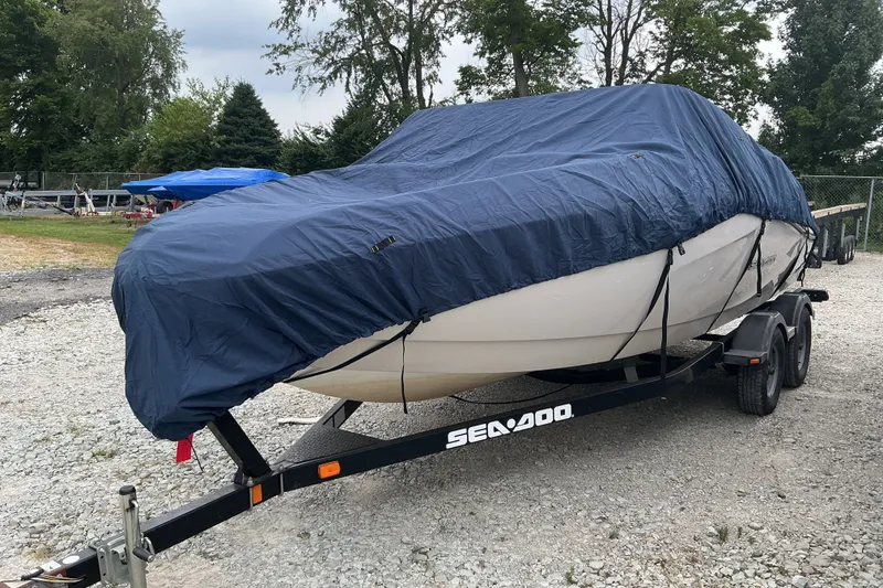 Slide: The Image of A 2010 Sea-Doo Sport Boat 210 Challenger SE, covered on a trailer, parked on a gravel lot. - 4