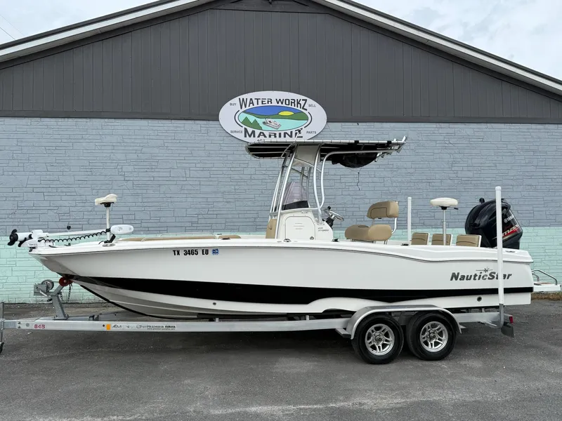 The Image of A white 2019 NauticStar 231 HYBRD CC boat on a trailer in front of a gray building. - 1