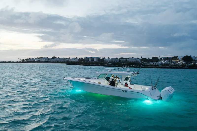 Slide: The Image of 2027 HCB 48 Campeon boat with glowing underwater lights on a serene ocean. - 2