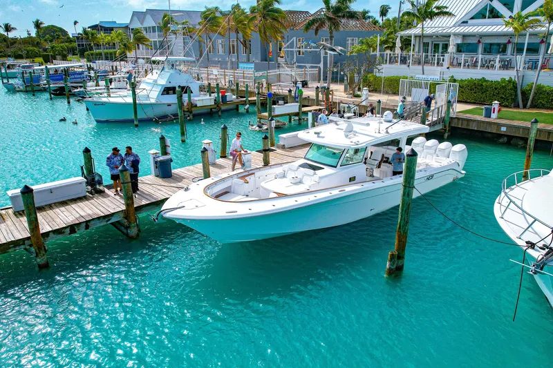 Slide: The Image of 2027 HCB 48 Campeon yacht docked in turquoise marina, surrounded by boats and waterfront buildings. - 1
