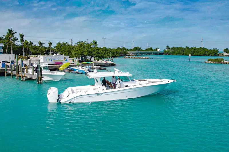 Slide: The Image of 2027 HCB 48 Campeon boat cruising in turquoise waters near a marina. - 0