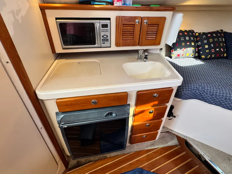 Slide: The Image of The cabin of a 2006 Pursuit 3370 Offshore features a compact kitchen with a microwave, sink, and cabinets. - 23