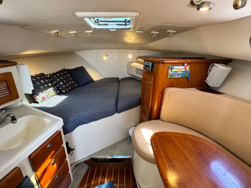Slide: The Image of The cabin of a 2006 Pursuit 3370 Offshore features a cozy bed, seating area, and small kitchenette. - 22
