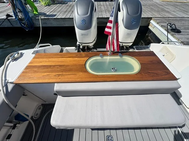 Slide: The Image of The image shows the stern of a 2006 Pursuit 3370 Offshore boat. There are two engines, a wooden countertop with an integrated sink, and an American flag. - 16
