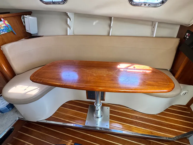 Slide: The Image of The interior of a 2006 Pursuit 3370 Offshore features a curved bench seat and a wooden table. - 21