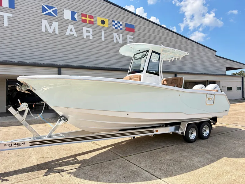 Slide: The Image of A 2027 Sea Hunt Ultra 265 SE boat on a trailer in front of a building with flags. - 2