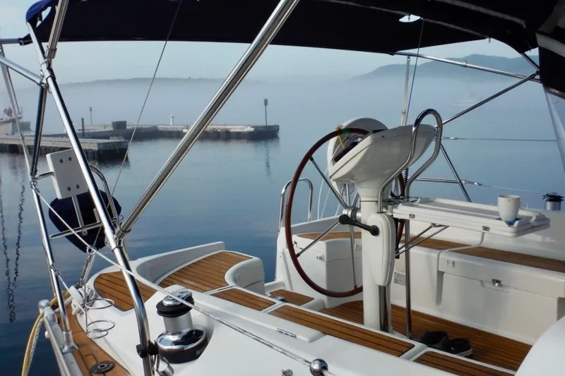 Slide: The Image of 2004 Jeanneau Sun Odyssey 37 sailboat cockpit with wooden deck, steering wheel, and misty harbor view. - 10