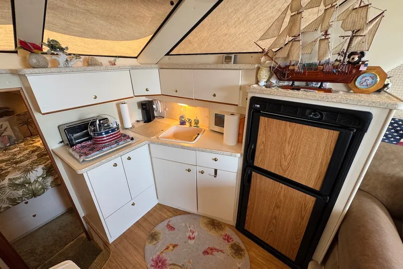 Slide: The Image of 1999 Silverton 351 Sedan yacht interior with kitchenette, featuring cabinets, sink, and decorative ship model. - 15