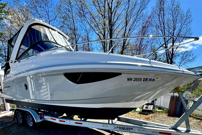 Slide: The Image of 2019 Regal 28 Express boat on trailer, parked outdoors with trees in background. - 2