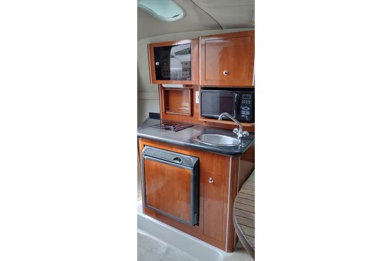 Slide: The Image of Compact kitchen area in a 2006 Doral Monticello 250 boat, featuring wood cabinetry and modern appliances. - 22