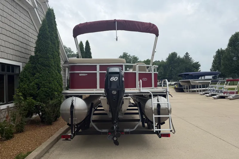 Slide: The Image of 2011 Harris Cruiser 220 pontoon boat with outboard motor, parked near a building. - 2