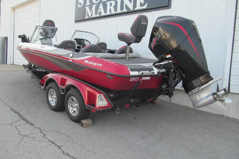 Slide: The Image of 2024 Ranger 212LS boat with dual-axle trailer, red and black design, parked outside marine store. - 3