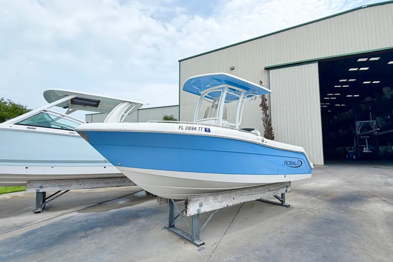 The Image of 2024 Robalo R222 Center Console boat in blue, displayed outside a large storage facility. - 0
