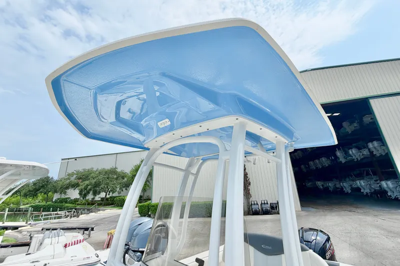 Slide: The Image of 2024 Robalo R222 Center Console boat with blue T-top, parked near a warehouse. - 25