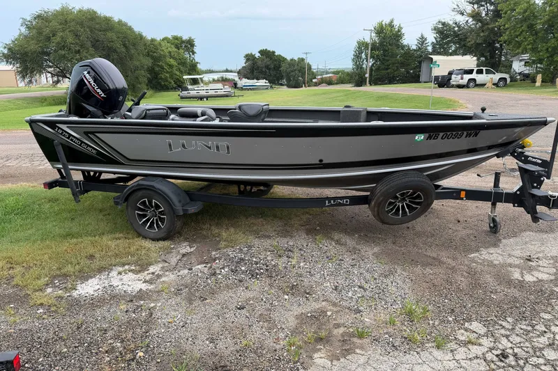 The Image of 2025 Lund 1875 Pro Guide fishing boat on trailer, parked on grassy area. - 1