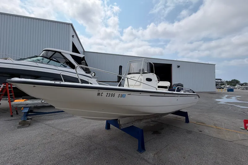 The Image of 2000 Boston Whaler 22 Dauntless boat on stand near warehouse, under cloudy sky. - 0