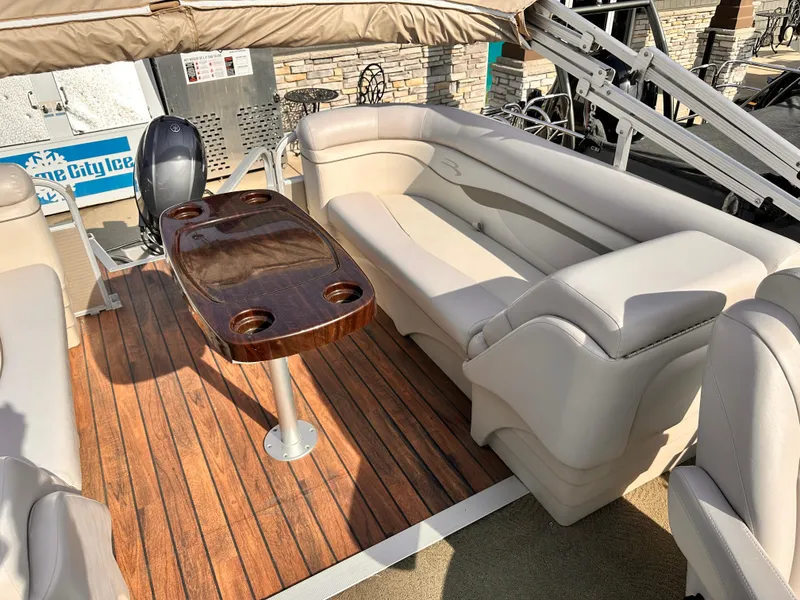 Slide: The Image of 2015 Bennington S24 boat interior with beige seating and wooden table. - 16